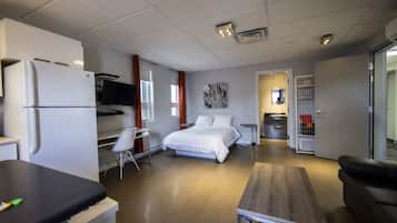 Ett modernt hotellrum med ett litet kök, en säng, ett skrivbord och en sittgrupp.