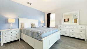 Une chambre à coucher comprenant un lit, des tables de chevet, une commode et un miroir.