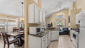 A spacious kitchen with white cabinetry, a dining area with wooden chairs, and a built-in oven. - Vibrant resort pool home with games room - Terra Verde (Kissimmee)