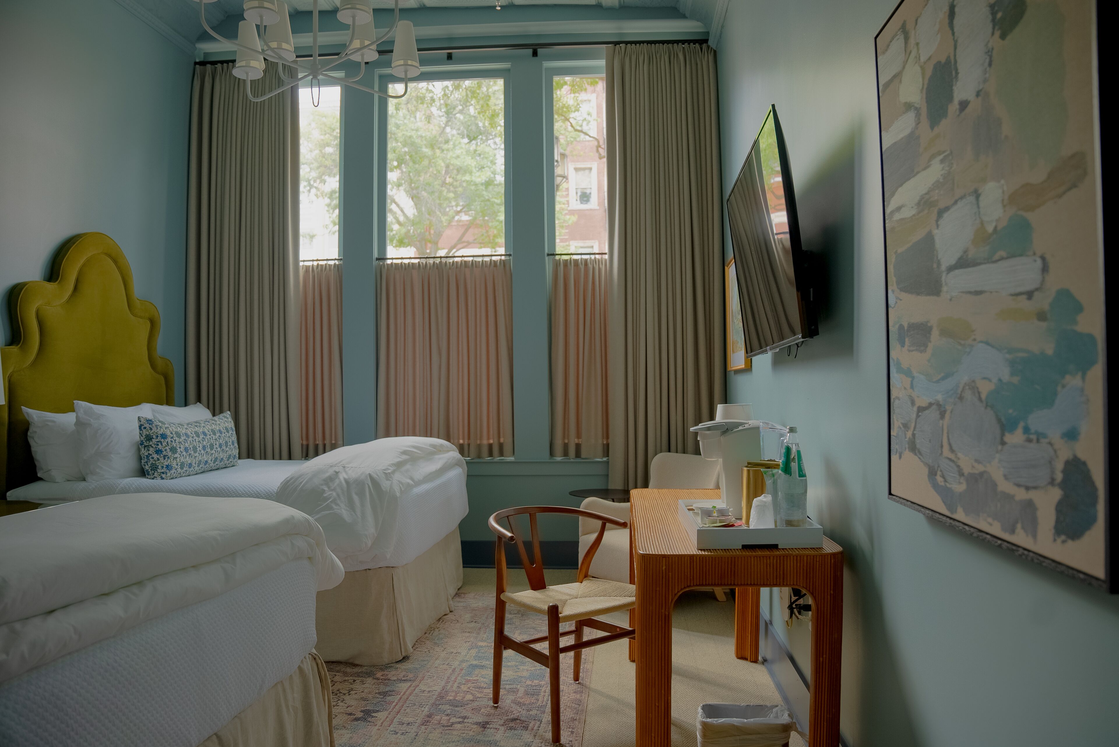 Camera d'albergo con due letti, una scrivania con una sedia, una televisione e una finestra con tende.
