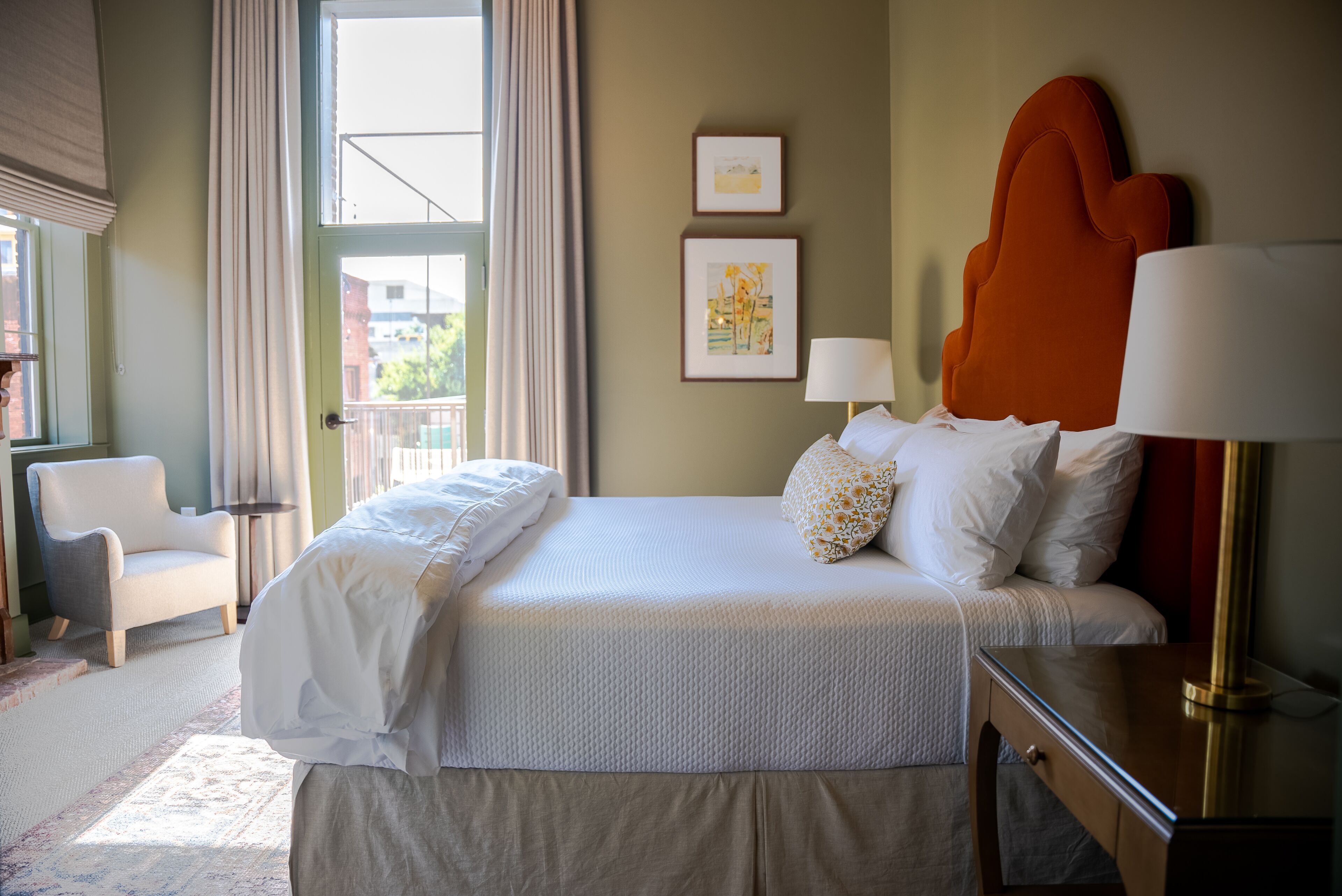 A hotel room with a bed, a chair, a nightstand, and a window with curtains.
