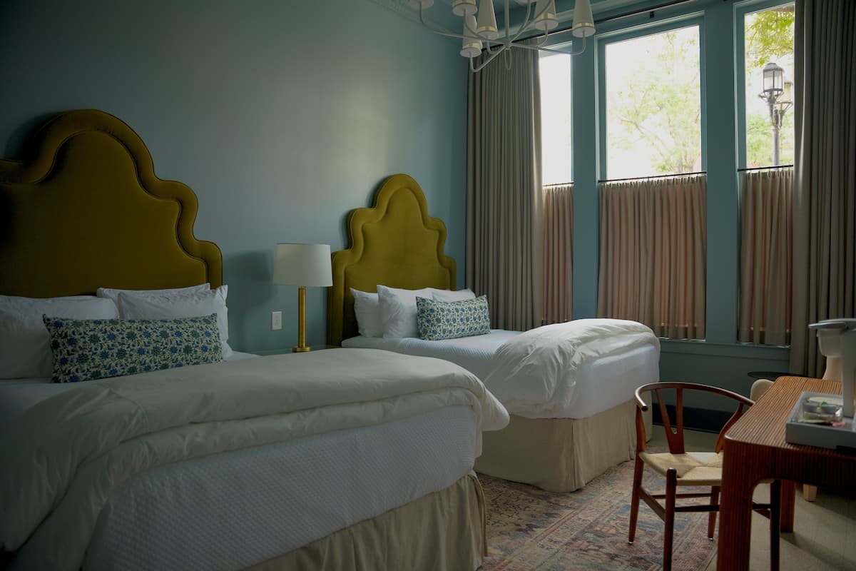 A hotel room with two beds, a small table, and a chair.