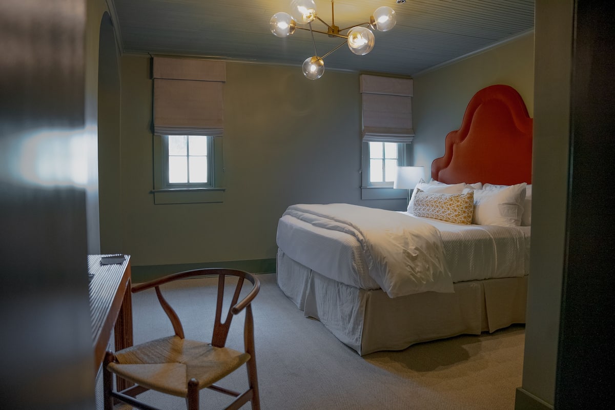 A bedroom with a bed, a chair, and a unique red headboard.