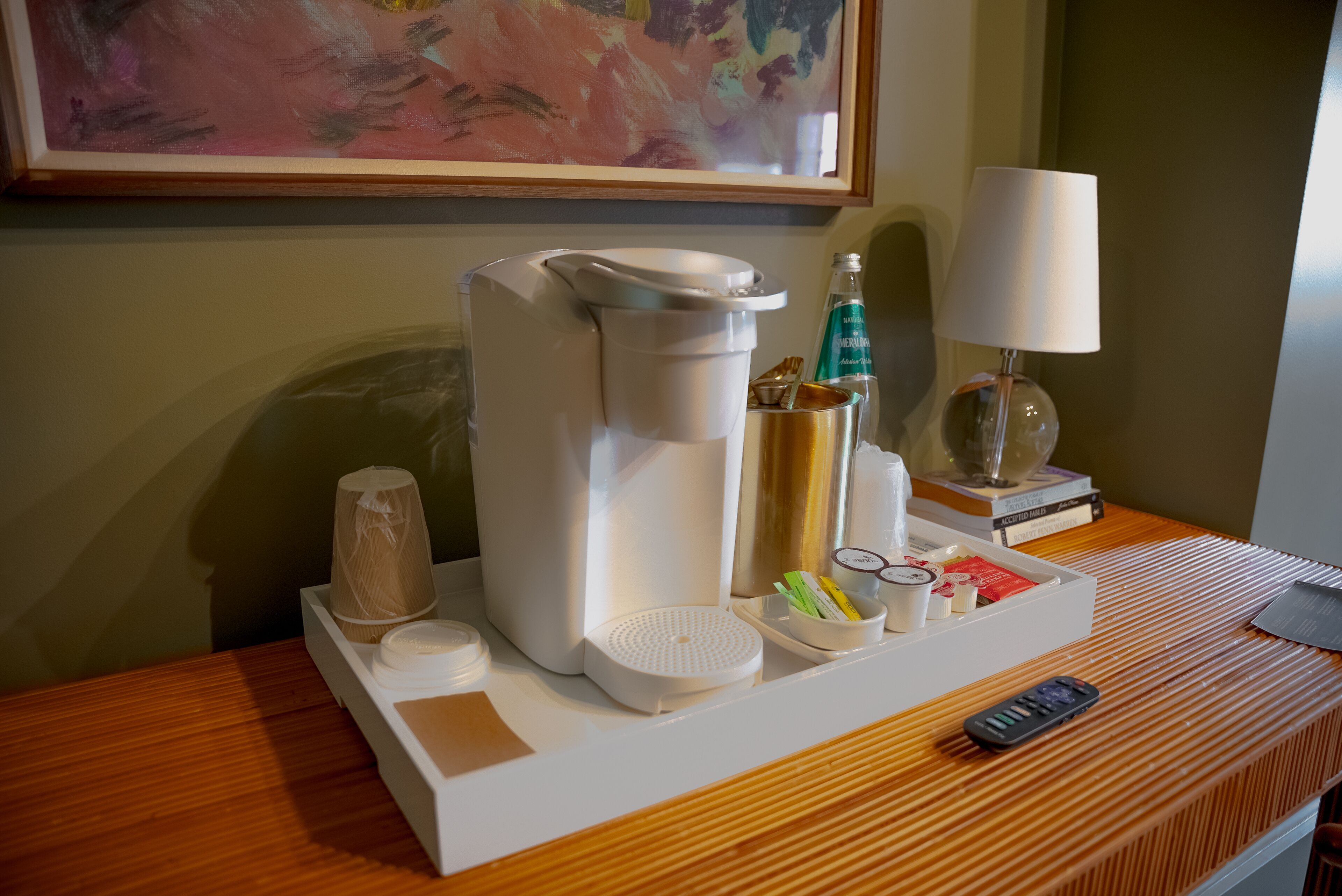 A hotel room with a coffee maker, a remote control, and a tray with various items including a bottle and a cup.