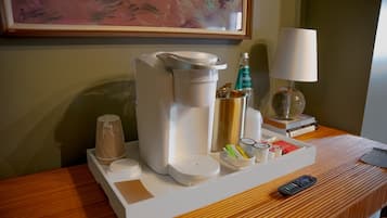 A hotel room with a coffee maker, a remote control, and a tray with various items including a bottle and a cup.