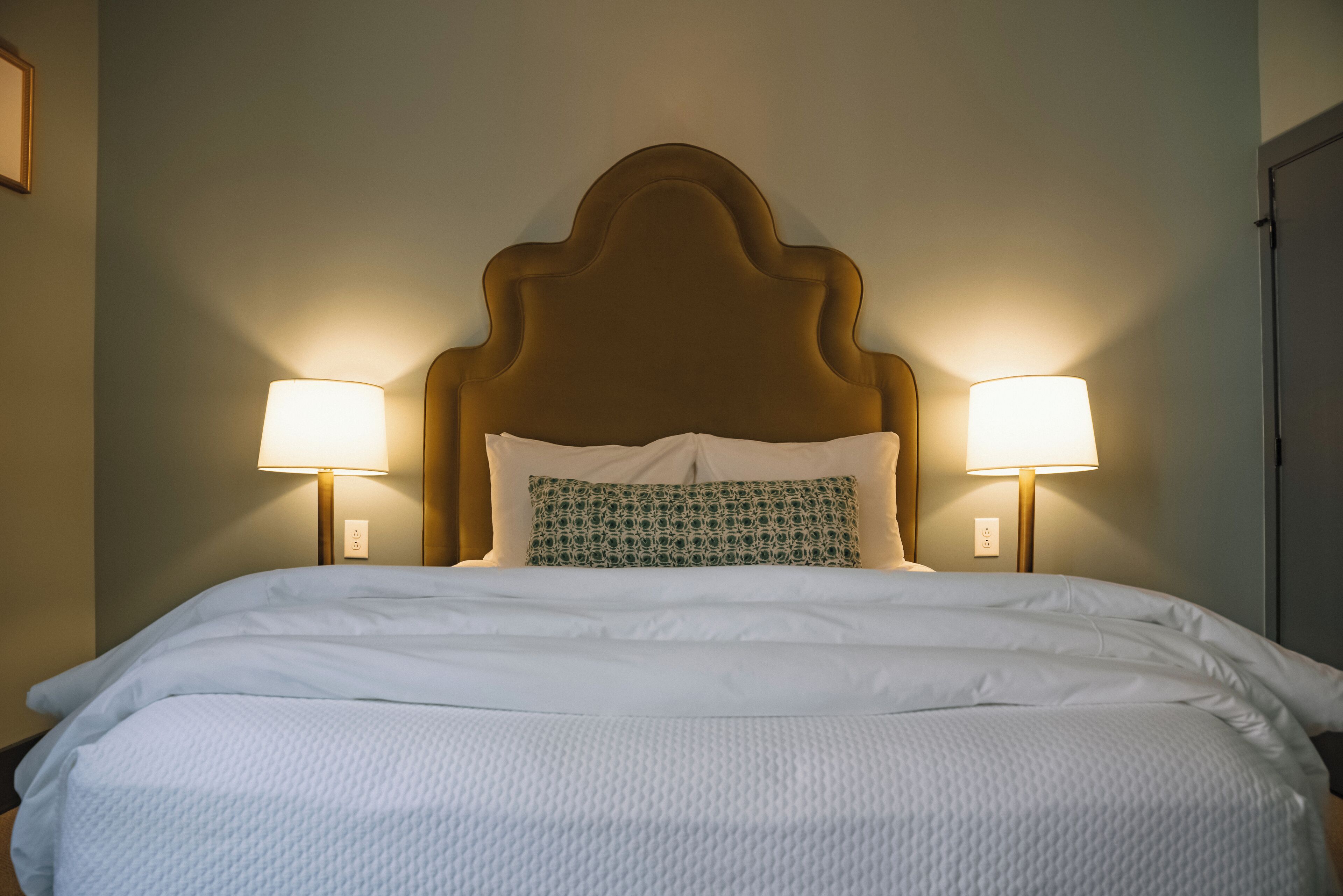 A neatly made bed with a wooden headboard, two bedside lamps, and a patterned pillow.