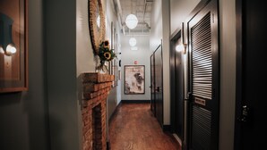 A hallway with a brick fireplace, wooden flooring, and doors on both sides. - The Woodward Hotel (Macon)