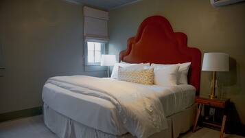 Een net opgemaakt bed met witte lakens, een rood hoofdeinde en een bedlampje.