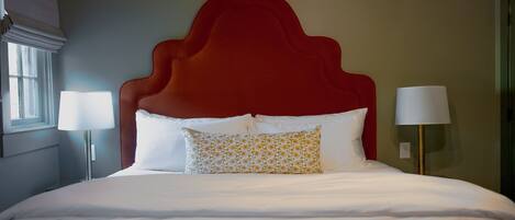 A hotel room with a large bed, two bedside lamps, a red headboard, and an air conditioning unit.