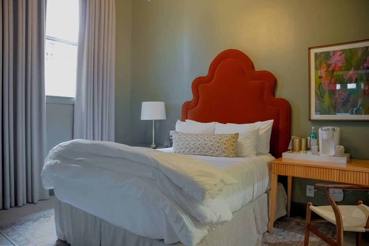 A hotel room with a bed, a desk, a lamp, and a painting on the wall.