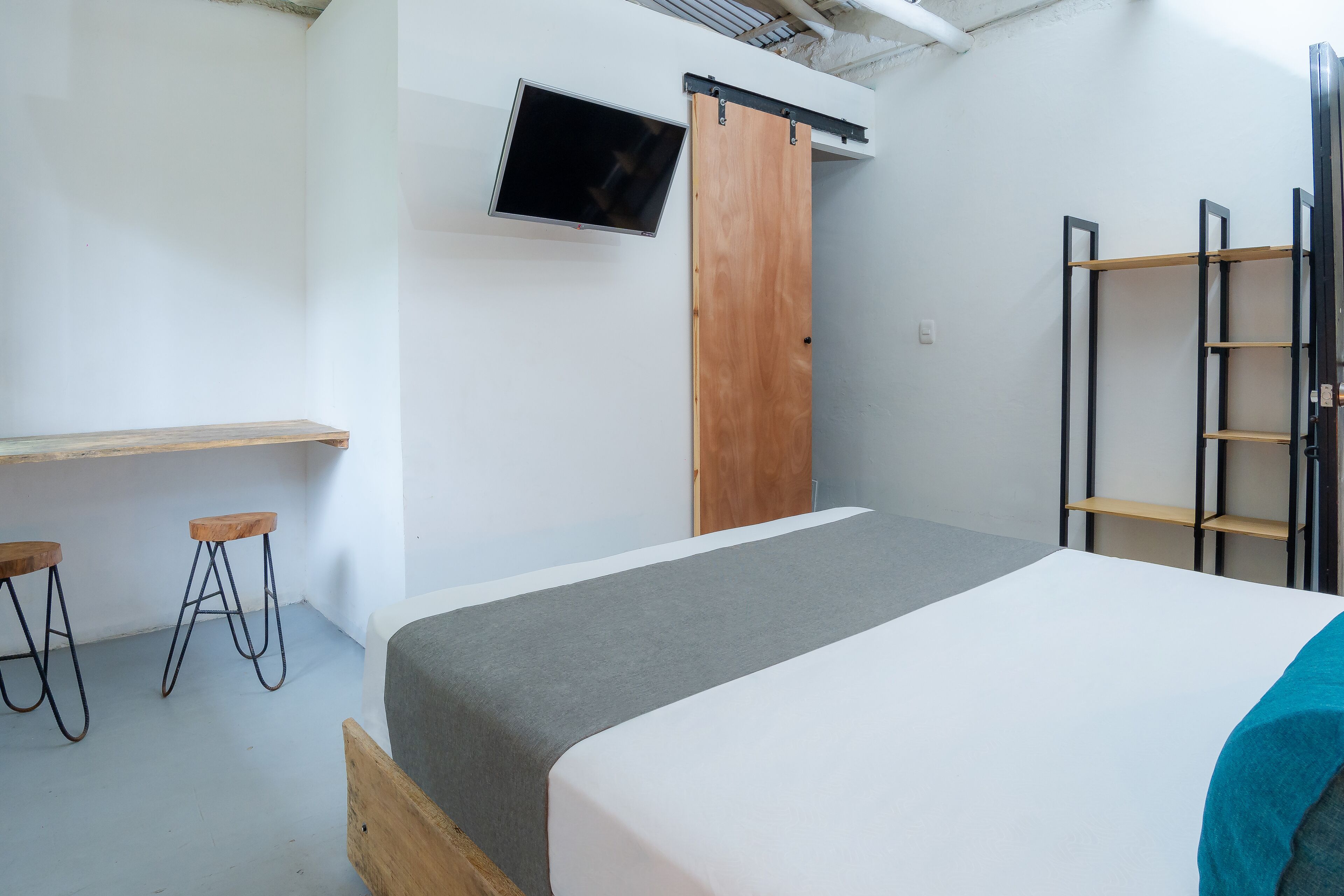 A bedroom with a bed, a TV mounted on the wall, a wooden wardrobe, and a ladder.