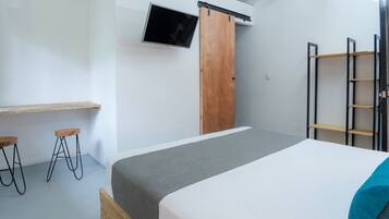 A bedroom with a bed, a TV mounted on the wall, a wooden wardrobe, and a ladder.