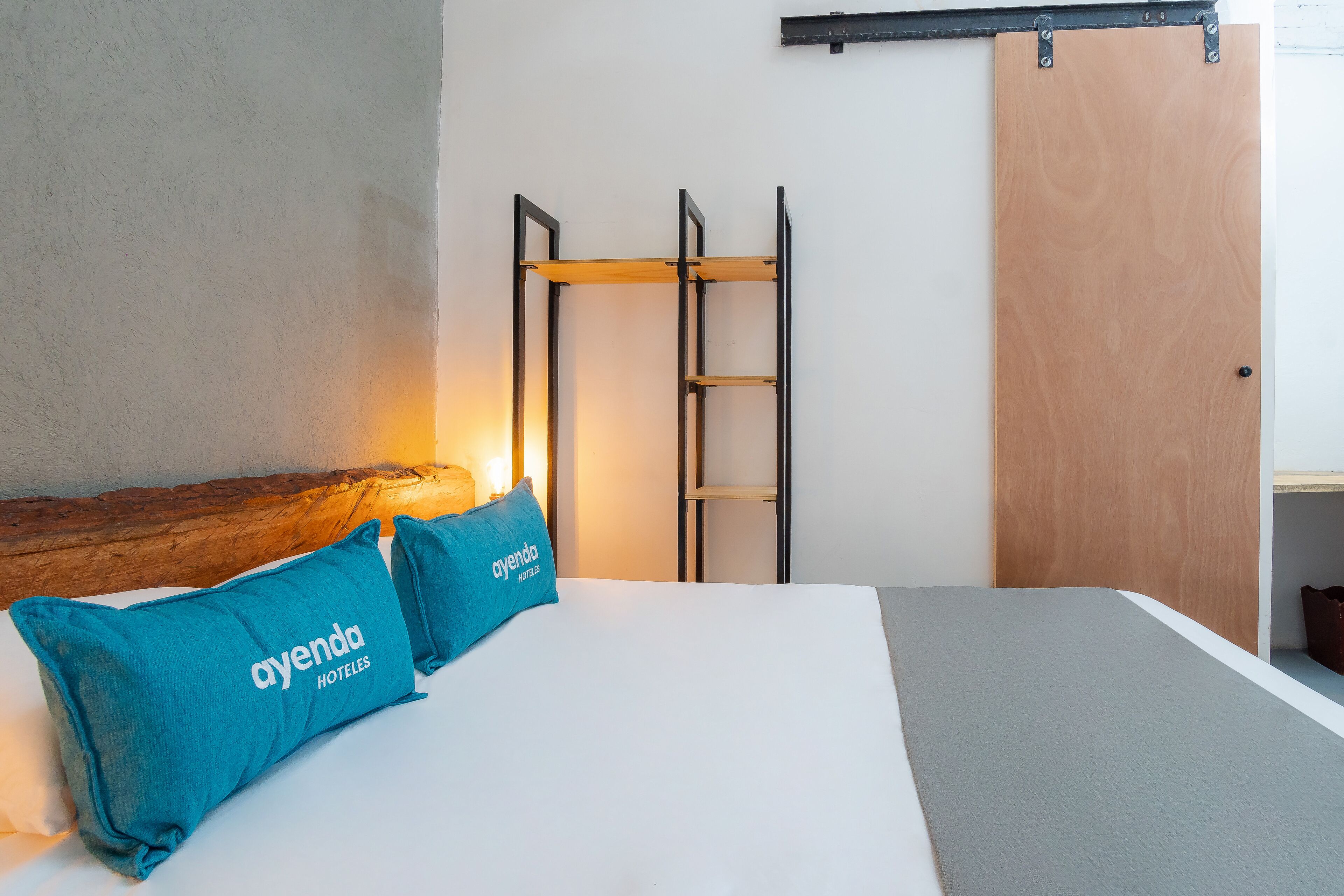 A hotel room with a bed, two blue pillows, a wooden headboard, a metal ladder, and a wooden door.