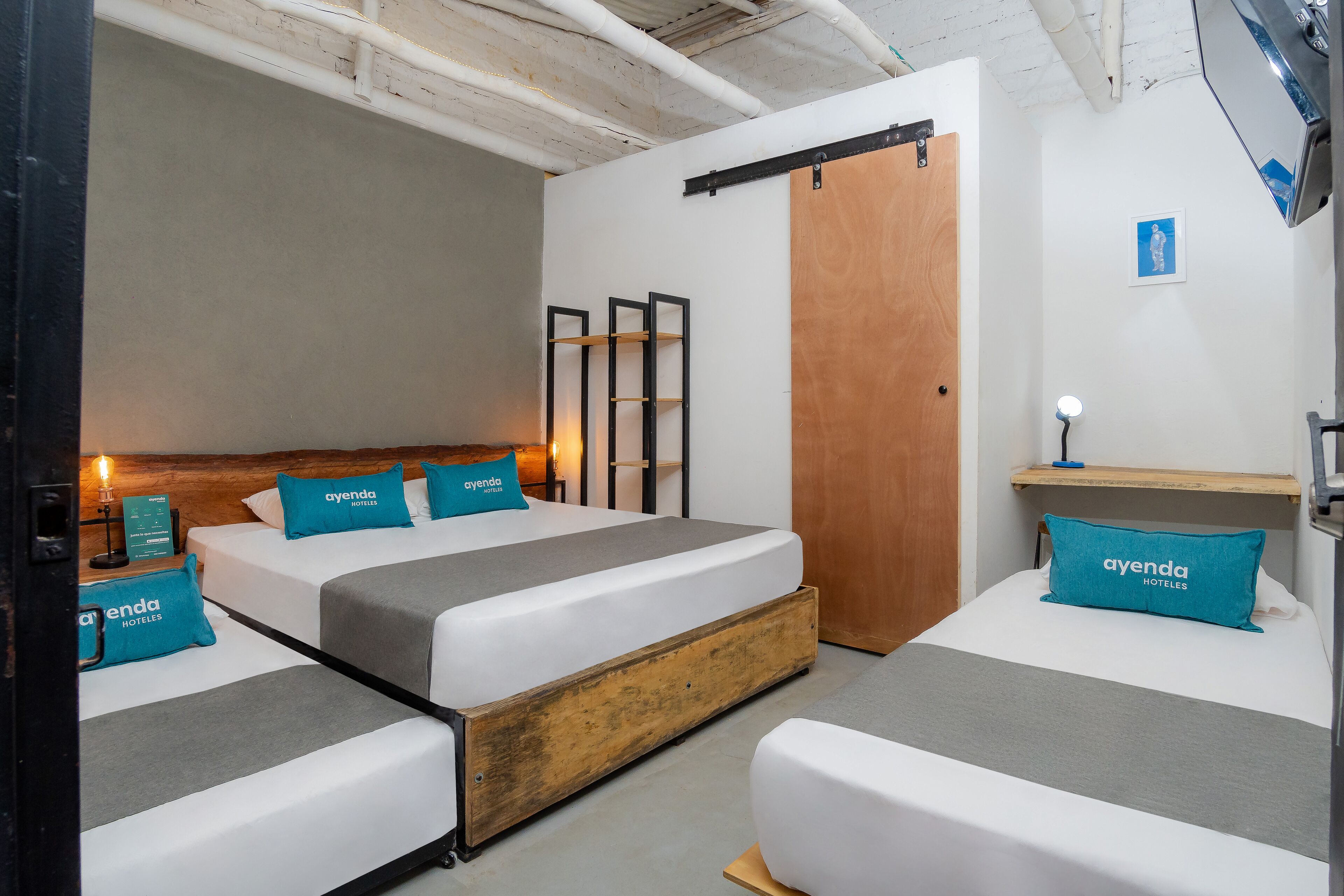 A hotel room with two beds, wooden headboards, and teal pillows with the hotel name.