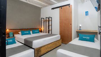 A hotel room with two beds, wooden headboards, and teal pillows with the hotel name.
