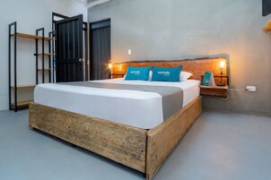 Un dormitorio moderno con estructura de cama de madera, ropa de cama blanca y dos almohadas azules con la marca 'ayenda hotels'.