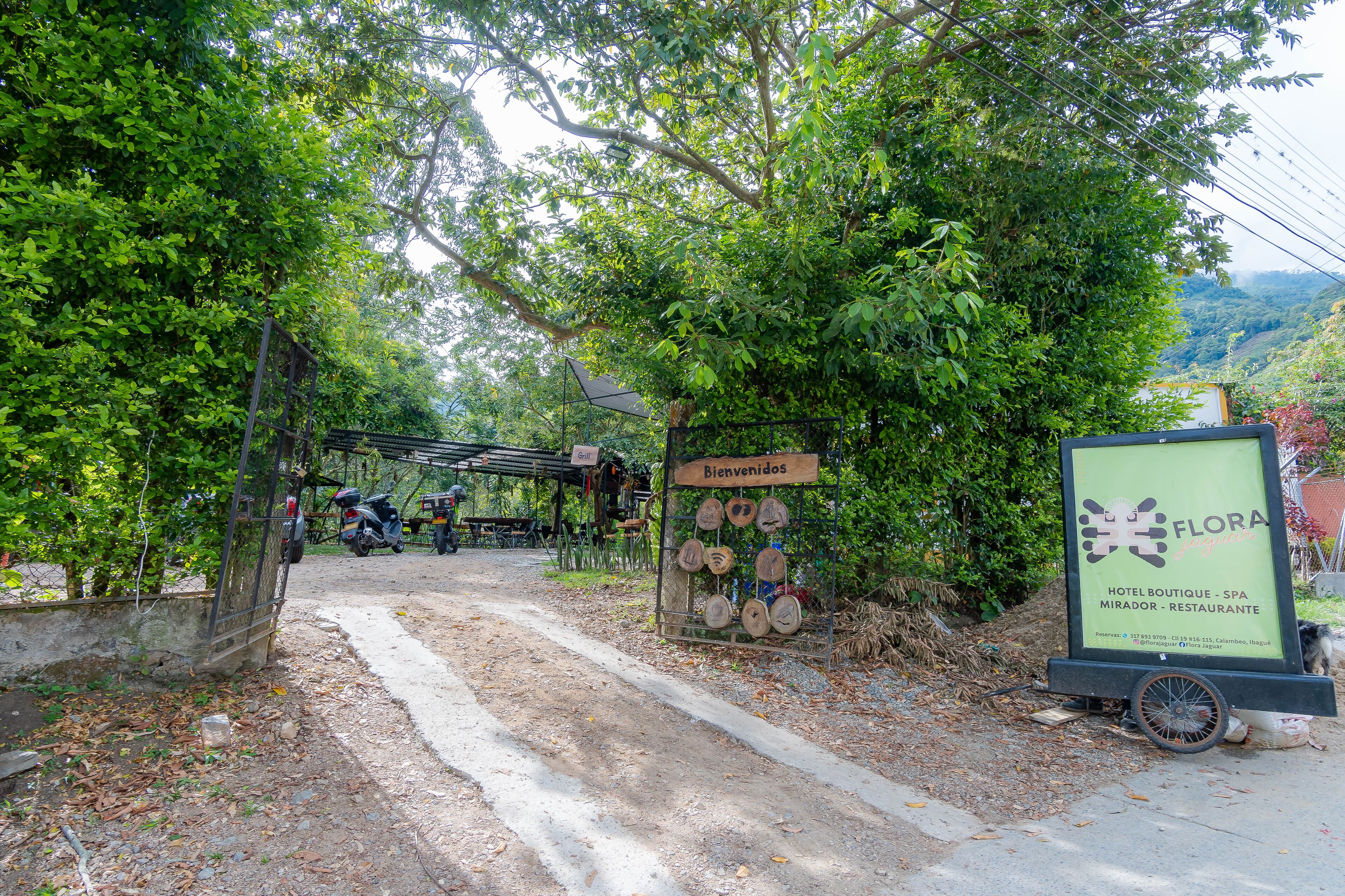 Schild für ein Hotel, eine Boutique-Spa und ein Restaurant mit rustikalem Holzbau, umgeben von üppiger Vegetation und einem Feldweg, der zum Eingang führt.