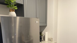 A modern kitchen with a stainless steel refrigerator, grey cabinets, a marble countertop, and a trash bin. - Stylish 1 Bedroom Apartment in Gadsden, AL (Gadsden)