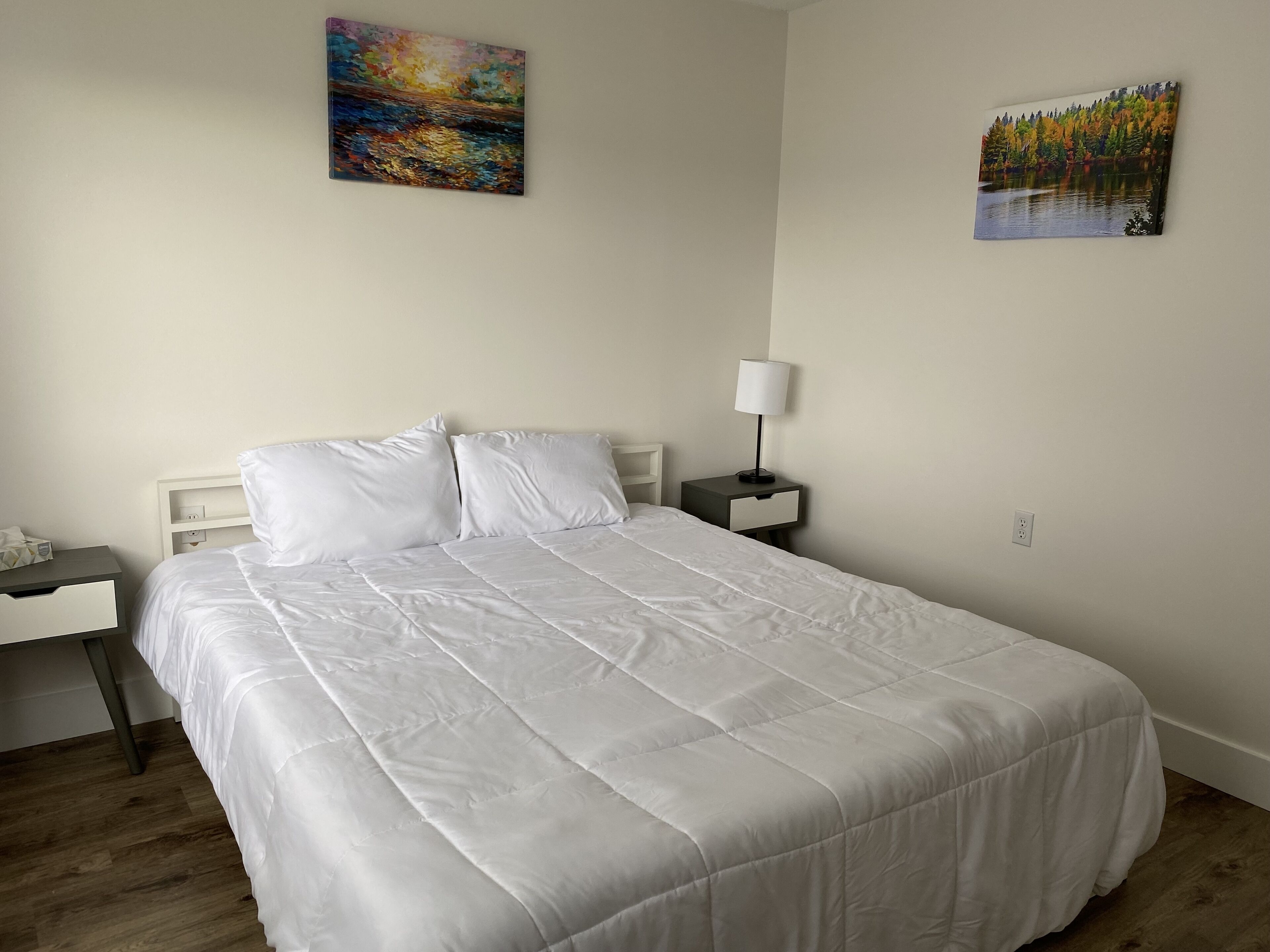A neatly made bed with white bedding in a room with a wooden floor.