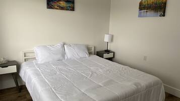 A neatly made bed with white bedding in a room with a wooden floor.