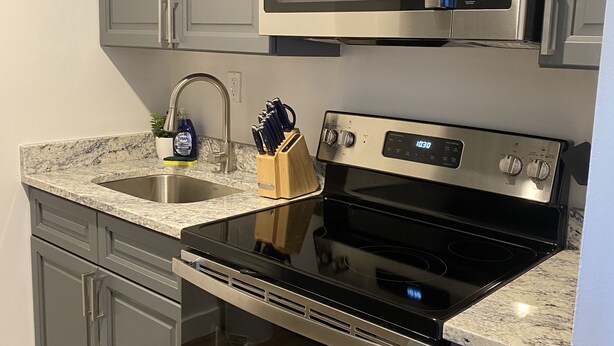 A kitchen with grey cabinets, a stainless steel microwave, a stove, and a sink. - Stylish 1 Bedroom Apartment in Gadsden, AL (Gadsden)