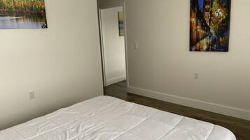 A bedroom with a white bedspread, a painting of a lake, and another painting of a night scene.