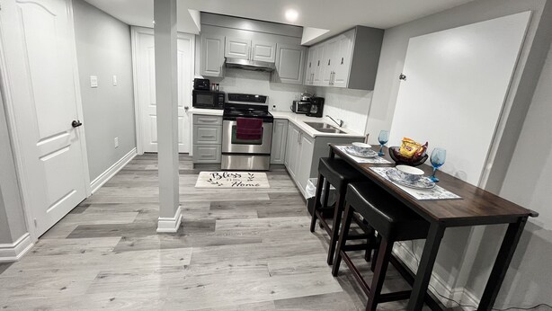 Una cocina moderna con gabinetes blancos, electrodomésticos de acero inoxidable y una mesa de comedor de madera con taburetes de bar.