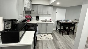 Una cocina compacta con armarios blancos, una estufa negra y un tapete de madera con texto.