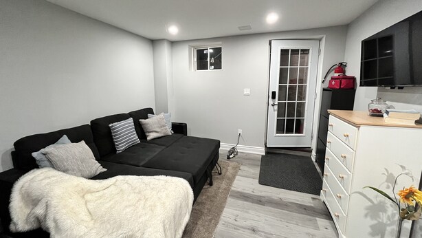 Un dormitorio moderno con un sofá negro, un aparador blanco y una puerta con panel de vidrio.