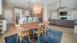 Een ruime keuken met een eethoek, houten stoelen, een blauw vloerkleed en een plafondventilator.