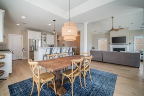 A spacious kitchen with a dining area, wooden chairs, a blue rug, and a ceiling fan.