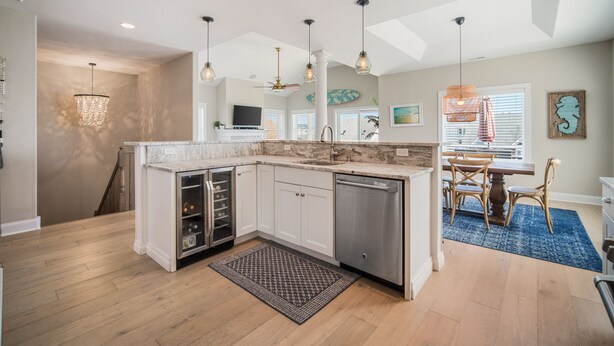 Een moderne keuken met witte kastjes, een vaatwasser en een ingebouwde wijnkoeler. Er is een eethoek met een tafel en stoelen, en een blauw vloerkleed.