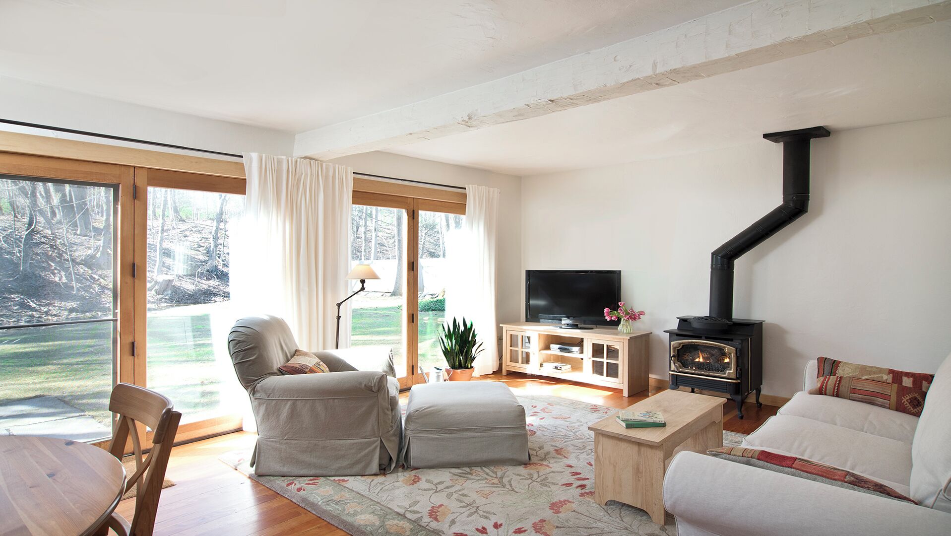 Un salón acogedor con chimenea, televisor y un ventanal grande con vistas a un jardín.