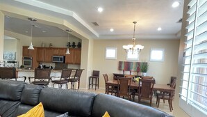 A modern living room with a dark leather sofa, a dining area, and a kitchen in the background.