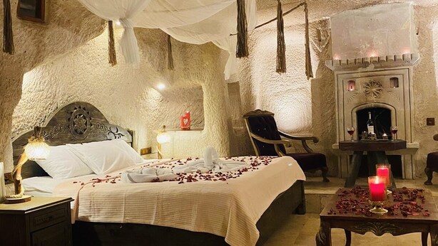 A cozy, rustic bedroom with a stone wall, a bed with a canopy, a fireplace, and a small table with candles. - Ela cave house (Ürgüp)