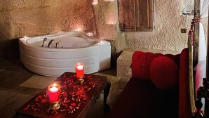 A cozy, dimly lit room with a stone wall, a large bathtub, a wooden cabinet, and a red sofa. - Ela cave house (Ürgüp)