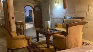 A rustic room with a bed, two armchairs, a wooden coffee table, and a hanging light fixture. - Ela cave house (Ürgüp)