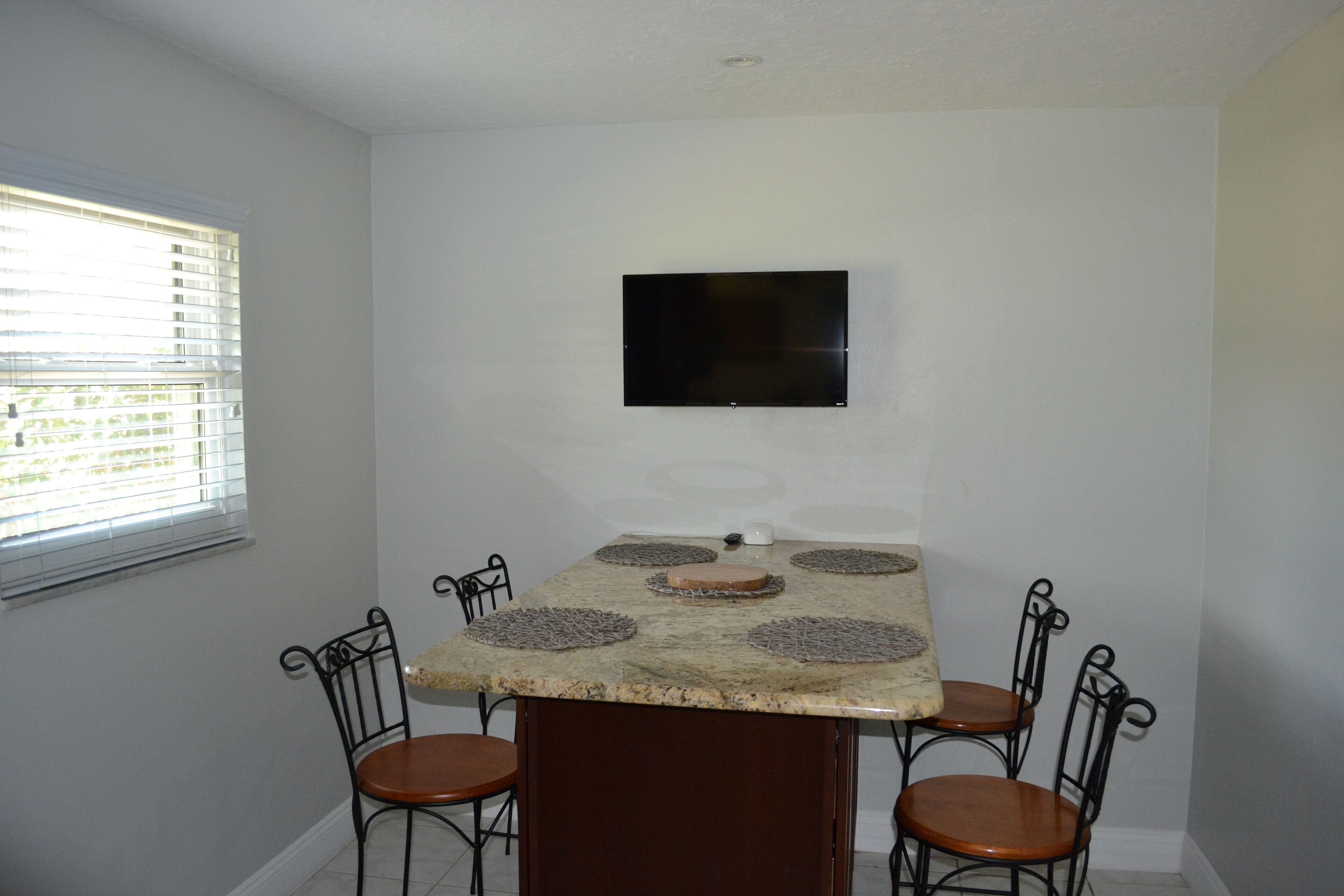 A dining area with a granite table, four chairs, and a flat-screen TV mounted on the wall.