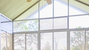 Ein Wintergarten mit Tisch und vier Stühlen, großen Fenstern und einem Deckenventilator.