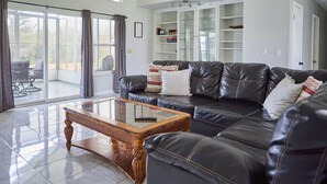 Ein geräumiges Wohnzimmer mit einem schwarzen Ledersofa, einem Glastisch und einer weißen Kommode mit Glastüren.