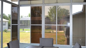 Ein überdachter Patio-Bereich mit Tisch und Stühlen, großen Fenstern und einem Deckenventilator.