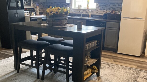 A modern kitchen with dark cabinetry, a central island with stools, a refrigerator, and a window with natural light.