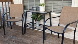 A wooden deck with two chairs and a small table, a potted plant, and a metal bucket.