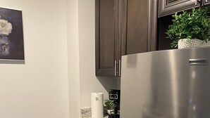 A modern kitchen with dark wooden cabinets, a stainless steel refrigerator, a marble countertop, and a trash can. - Sophisticated Studio Apartment in Gadsden, AL (Gadsden)