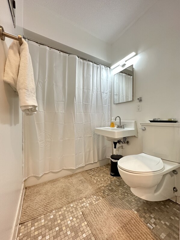 A bathroom with a toilet, sink, and shower curtain. - Sophisticated Studio Apartment in Gadsden, AL (Gadsden)