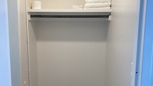 A small, narrow hallway with a wooden floor, white walls, and a shelf with towels and toilet paper. - Sophisticated Studio Apartment in Gadsden, AL (Gadsden)