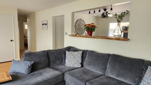 A grey sectional sofa with patterned cushions, a decorative mirror with a wooden shelf above, and a welcome sign on the wall. - Cozy Comfy (Bourbonnais)