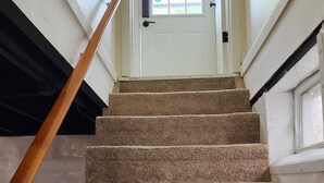 A carpeted staircase leading to a door with a window, a handrail on the left, and a doorbell on the right. - Cozy Comfy (Bourbonnais)