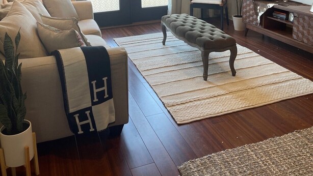 A living room with a sofa, ottoman, TV, and a large window with curtains. - Upscale condo centrally located in Baton Rouge!! (Baton Rouge)