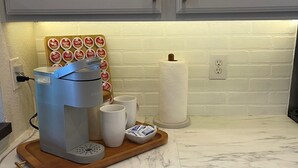 A kitchen with white cabinets, a coffee maker on a wooden tray, and a white brick backsplash. - Upscale condo centrally located in Baton Rouge!! (Baton Rouge)